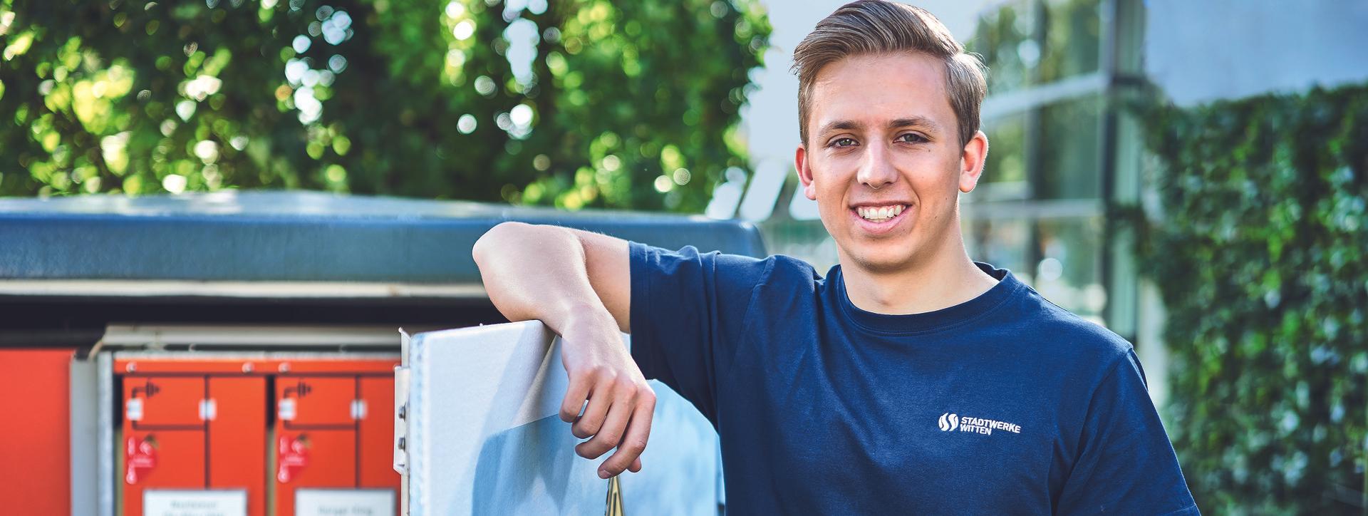 Azubi mit Stadtwerke T-Shirt lehnt an Spannungskasten